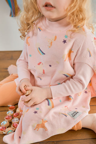 Boo Lätzchen mit Ärmeln Rainbow Dust: Kleinkind im rosa Lätzchen sitzt auf dem Holzboden, von nah
