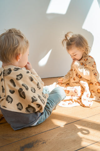 Boo Lätzchen mit Ärmeln Dessert Dune: zwei Kleinkinder sitzen auf dem Holzboden, eines trägt das Lätzchen