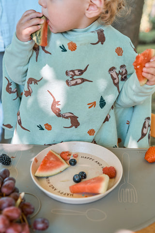 Boo Lätzchen mit Ärmeln Otter II: Kleinkind im Lätzchen isst Wassermelone am Tisch, von vorn