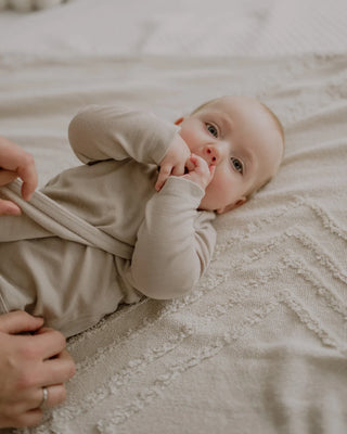 Qookie Wickelbody aus Wolle-Seide: Baby im beigen Body liegt auf einer Decke