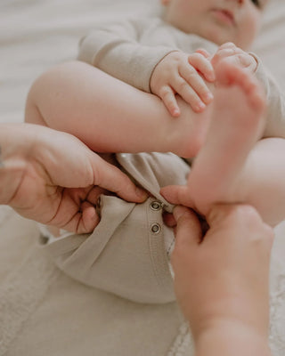 Qookie Wickelbody aus Wolle-Seide: Hände schließen die Druckknöpfe im Schritt am Baby