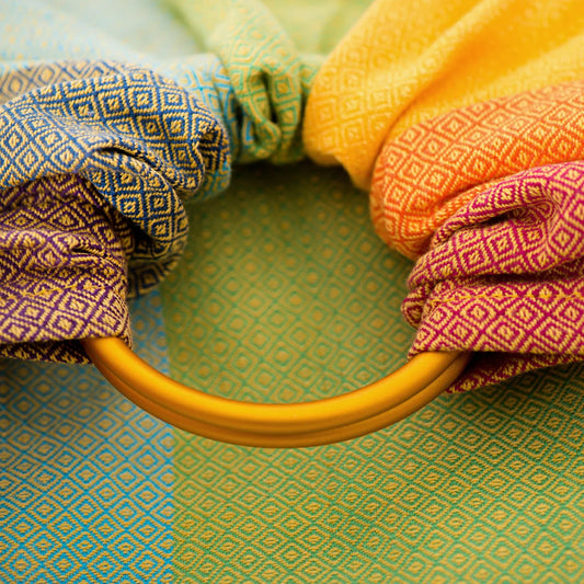 Warmer Schimmer und genialer Halt! Der handgewebte Ring Sling in den """"Gold Rainbow"""" Farben ist besonders griffig und ideal ab Geburt bis ins Kleinkindalter.""